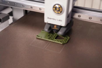 Drukarka 3D Bambu Lab A1 mini drukuje podstawkę na telefon z zielonego filamentu