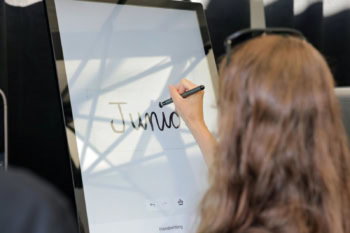 Klientka wpisuje odręcznie imię rysikiem na ekranie wolnostojącego kiosku xTool